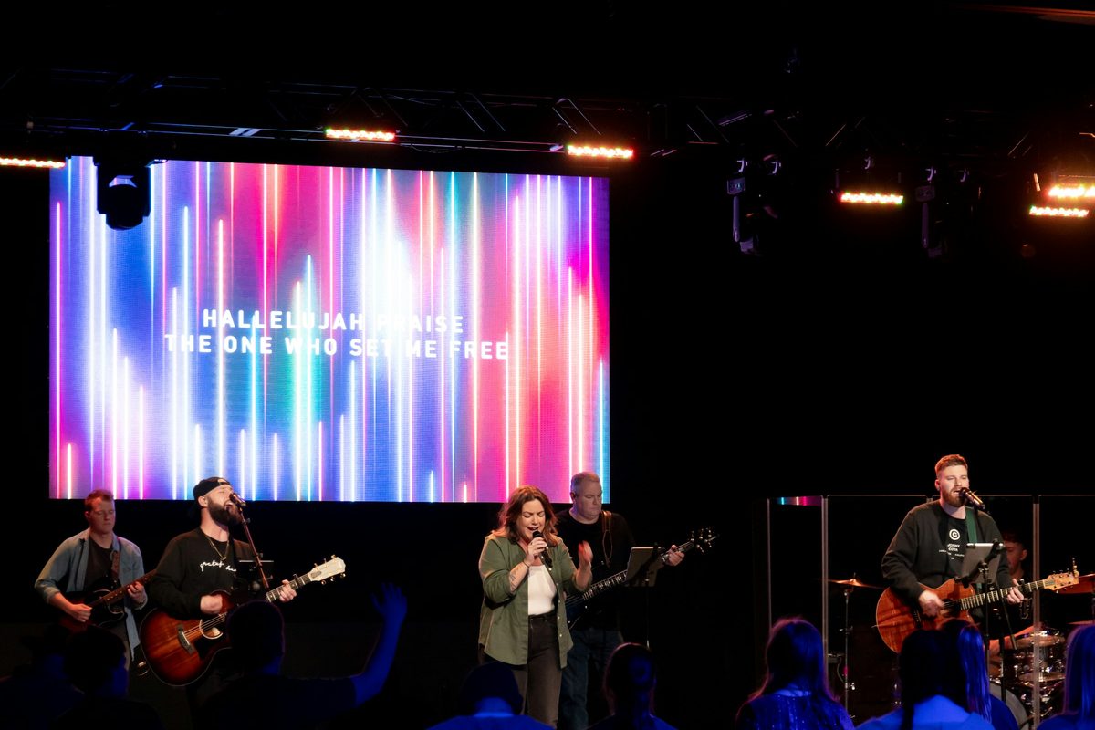 A worship band in a smaller room, song words on a bright LED wall behind them
