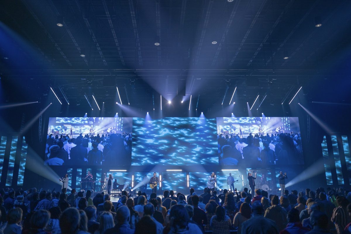 A wide LED wall across the stage, with side screens and beams of light over a full room